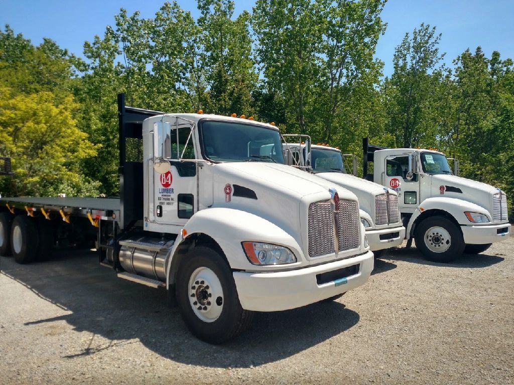 Three white BLS Trucking flatbed trucks parked in a row